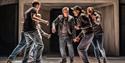 Punch - Six people in dark clothing gather close together in a circle. They are caught mid-action, jumping and moving, with excited expressions.