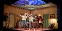 The Children - Three people in casual clothing are in front of a wooden table in a cross-section of a kitchen. They raise their arms and are moving, s
