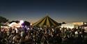 Photo of a crowd at riverside festival, in groups sat on benches and enjoying the stalls.