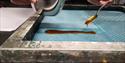 A person holding a bowl ink and a spoon, spreading this onto a printing screen