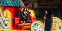 Three people smiling on a giant sleigh and waving at the camera
