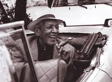 Edgar Macías smiling in back seat of open top car smoking a cigar