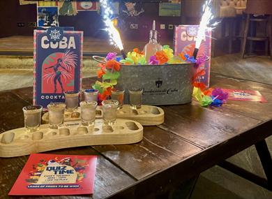 Photo of a bar table with cocktails in wooden trays, drinks menus and sparklers