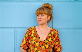 Sara Oschlag stood infront of a blue wall wearing a floral top