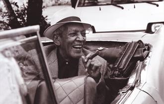 Edgar Macías Quintet, smiling, smoking cigar in a covertible car.