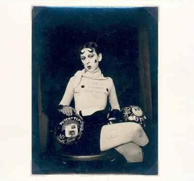 Portrait by Claude Cahun of a lady sat on a chair cross legged.