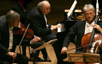 Photo of the Guarneri Trio on stage, playing their instruments