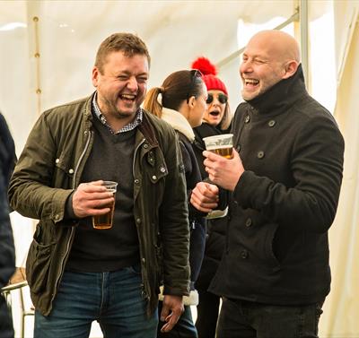 Photo of two men in a better trent, pints in hand, laughing and smiling.