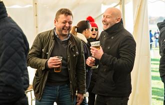 Photo of two men in a better trent, pints in hand, laughing and smiling.