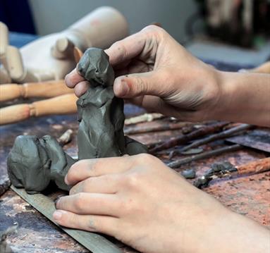 Image shows a pair of hands creating a piece of sculpture. 
