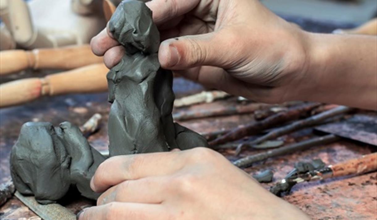 Image shows a pair of hands creating a piece of sculpture.