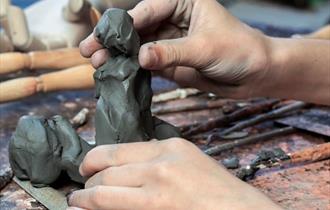Image shows a pair of hands creating a piece of sculpture.