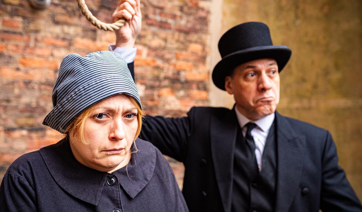 Two costumed actos recreating the scene of a woman at the gallows, with a noose about to be tied around her neck