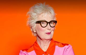 Photo of Jenny Eclair in front of a vibrant orange background
