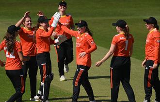 A photo of the women's cricket team ont he pitch. They are hi-5ing one another.