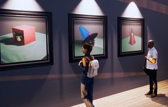 The image shows two people looking at three paintings on the wall.
