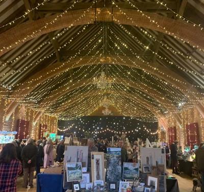 An indoor hall adorned with string lights for a warm and cosy atmosphere.You can see tables laid in the shape of market stalls, with arts and crafts f