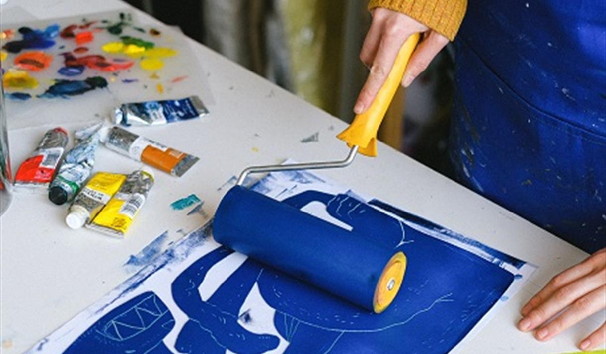 The image shows someone rolling blue paint on some paper using a paint roller.