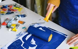 The image shows someone rolling blue paint on some paper using a paint roller.