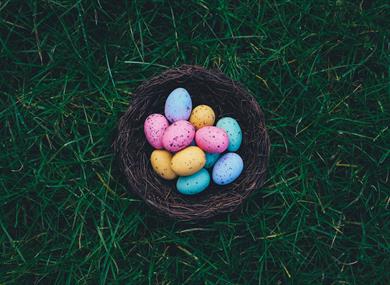 Photo of colourful easter eggs in a wicker basket.