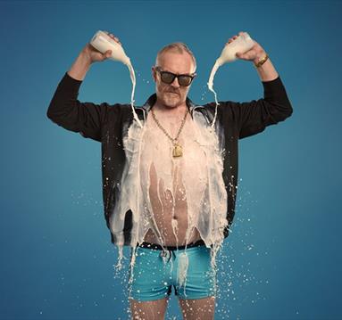 Show poster for Greg Davies new show showing him in underpants with an open shirt, pouring milk on himself.