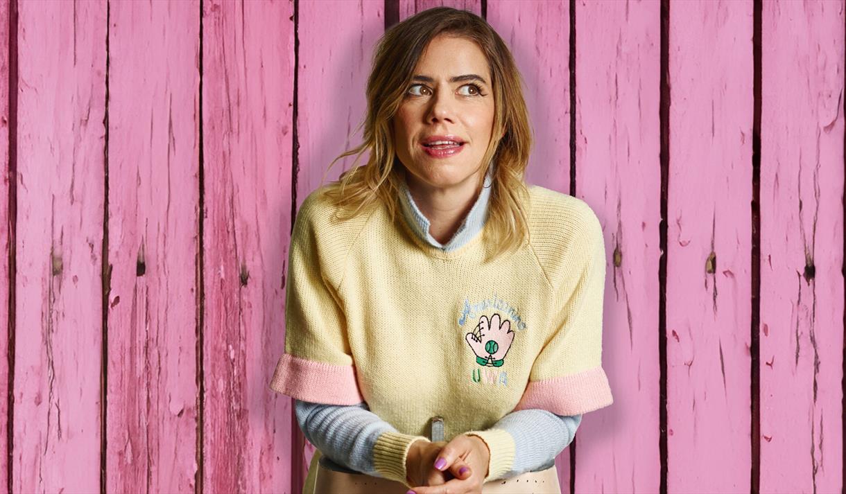 Photo of Lou Sanders in front of a wooden backdrop which is painted pink