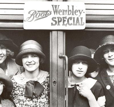 Old black and white photo of a group of women, taken through a set of glass doors, presumably at a Boots storefront.