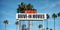 A sign surrounded by palm trees which says, "Drive-in movies, open".