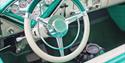 The steering wheel of a turquoise retro car.