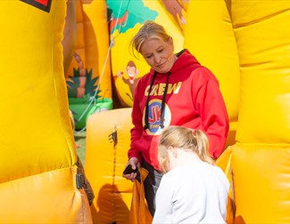 Jk Events crew staff member looking down at a child going into an inflatable