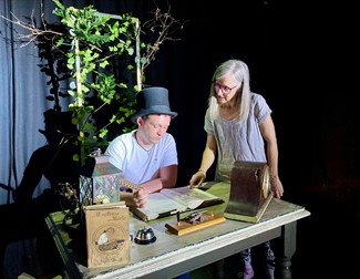 Two actors behind a desk looking at book on the desk