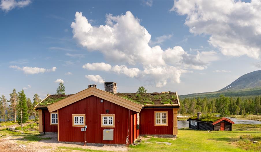 Tradisjonell hytte med torvtak, på hyttetun i fjellandskap ved innsjø