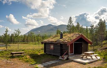 Tømmerhytte med torvtak i fjellandskap