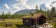 Tømmerhytte med torvtak i fjellandskap