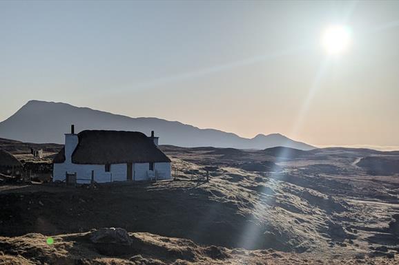 Sun shine on Glaic Cottage with hill behind.