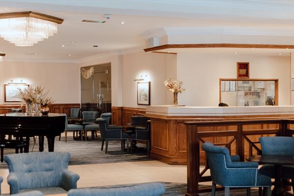 Lobby and reception desk at the Cabarfeidh Hotel in Stornoway with blue chairs and grand piano.