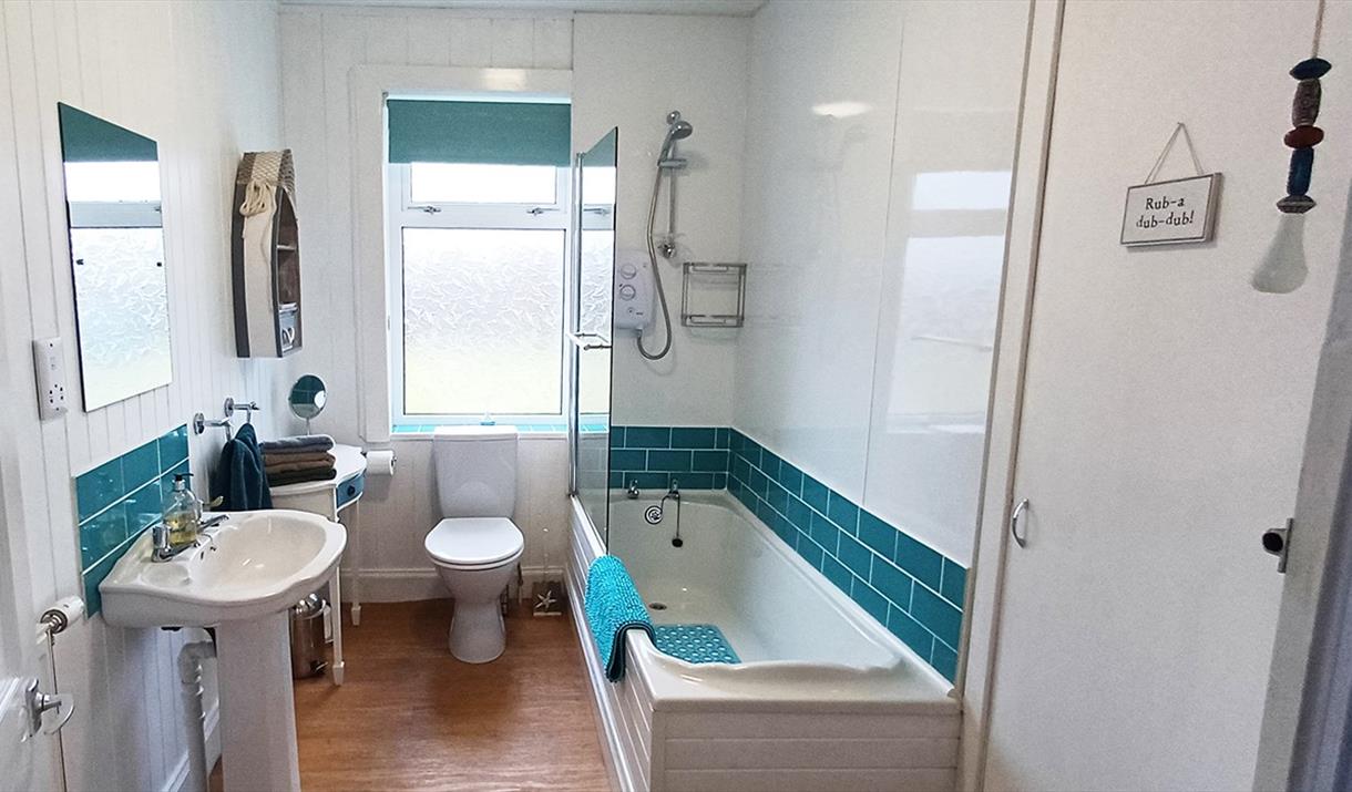 Bathroom Viewed from the hallway, Showing Bath with wall mounted shower unit, Toilet, Sink and Side Table.
