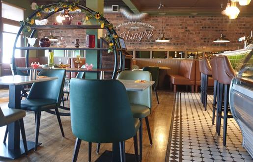 HS1 cafe bar interior with table and charis in a tan and teal colourway and exposed brick wall at rear.