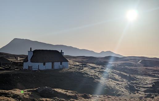 Sun shine on Glaic Cottage with hill behind.
