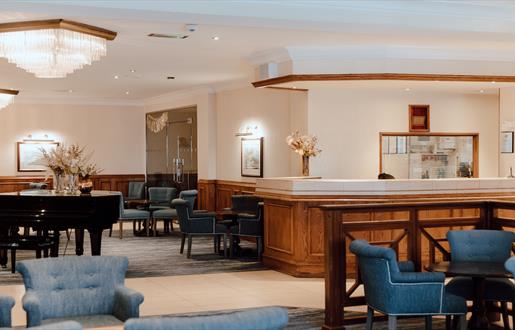 Lobby and reception desk at the Cabarfeidh Hotel in Stornoway with blue chairs and grand piano.