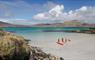 Three individuals on a beach with kayaks, preparing to explore the clear waters of the Isle of Barra by sea kayaking.