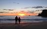 A young couple are standing on the shoreline watching the sun sink below the horizon, at Mangersta Beach, Isle of Lewis.