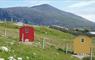 A red Shepherd's Hut and a yellow Shepherd's Hut in a wild flower meadow with a rocky hill (Mealaisbhal) in the background.