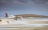 A Loganair plane landing on the beach runway at Isle of Barra, with the picturesque island in the background.