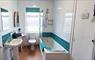 Bathroom Viewed from the hallway, Showing Bath with wall mounted shower unit, Toilet, Sink and Side Table.