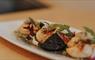 A white plate with neatly arranged Hebridean scallops, Stornoway black pudding, and mixed greens on a wooden surface.