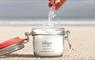 Hand sprinkling ishga Invigorating Bath Salts from an open jar on the beach