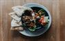 A bowl of vegan salad and flat bread on a wooden table.