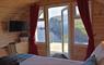 The view out from a SEApod across the ocean to the sea cliffs.  A fresh white bed in the foreground with colourful tweeds.  A folded dining table and