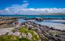 Rocky coastine in the Outer Hebrides with small orange boat, blue skies and crystal clear water.